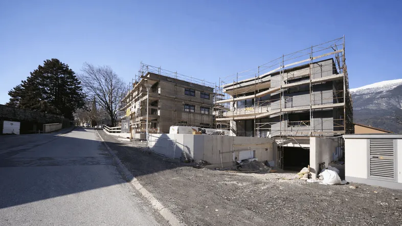 Neubauwohnungen im Bau mit Gerüst und Blick auf die umliegende Berglandschaft.