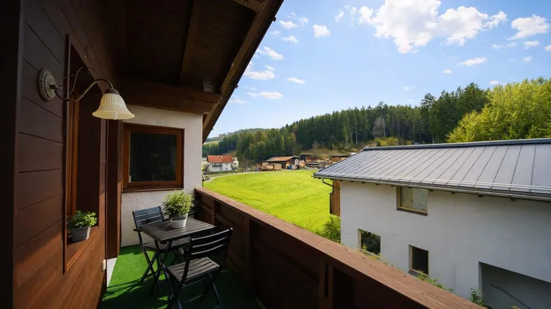 Sonniger Balkon mit Sitzgelegenheiten und weitem Blick über grüne Wiesen und Wälder.