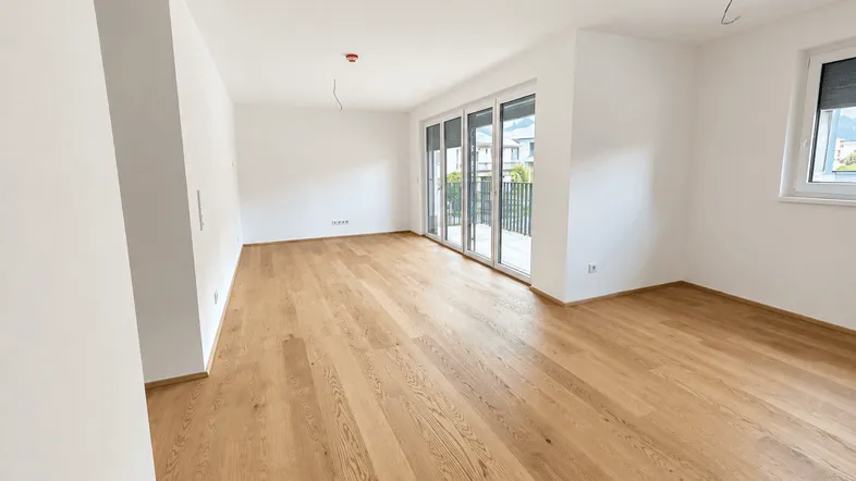 Helles Wohnzimmer mit Holzboden und großen Schiebetüren, die zu einem Außenbereich führen.