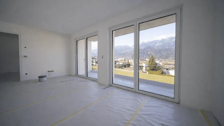 Heller, unmöblierter Wohnraum im Rohbau mit großen Fenstern und Bergblick.