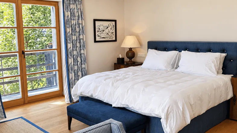 Helles Schlafzimmer mit blauem Bett, passenden Sesseln und Zugang zu einem französischen Balkon.