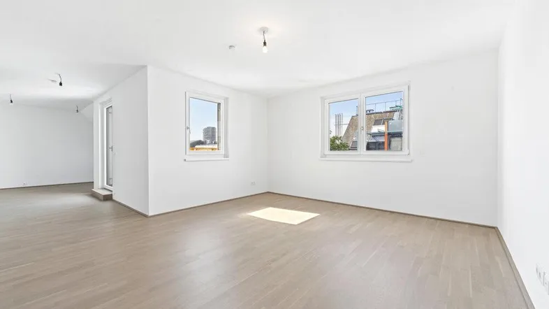 Helles Zimmer mit Parkettboden und zwei Fenstern, das viel Tageslicht hereinlässt.