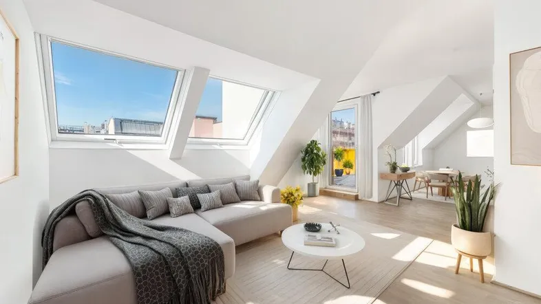 Helles Wohnzimmer mit Dachfenstern, Schrägdach und modernem Sofa, offen zum Essbereich.