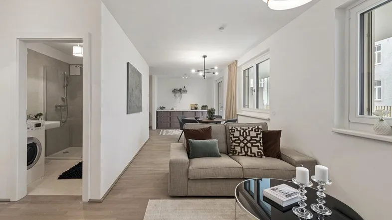 Heller offener Wohn- und Essbereich mit modernem Sofa, Holzboden und Zugang zu einem Badezimmer.