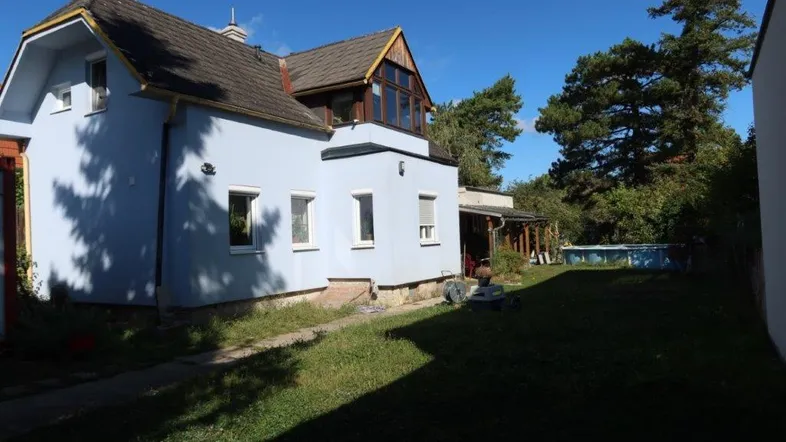 Blau gestrichenes Einfamilienhaus mit Garten, Rasenfläche und einem kleinen Aufstellpool im Freien.