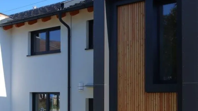 Moderne Hausfassade mit weißem Putz, dunklen Akzenten und Holzverkleidung.