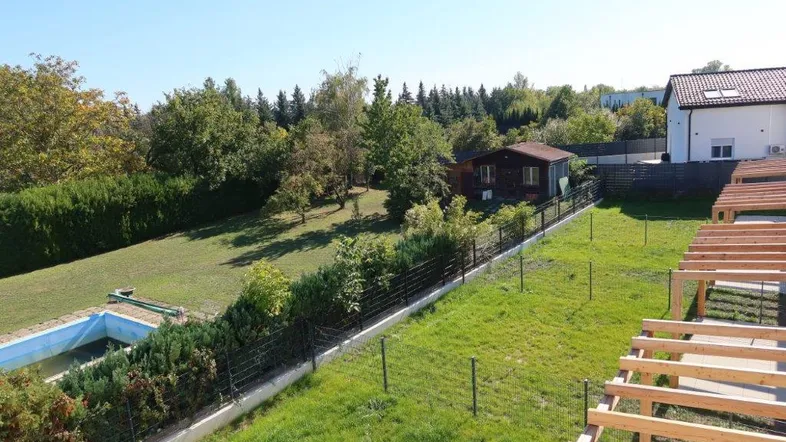 Weitläufiger Gartenbereich mit Swimmingpool, Rasenfläche und einem Gartenhaus unter blauem Himmel.