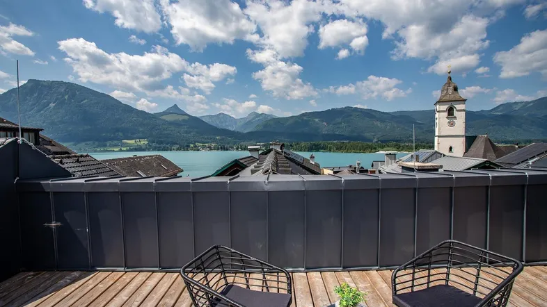 Große Dachterrasse mit Holzboden, Sitzgelegenheiten und atemberaubendem Blick auf den See und die Berge.