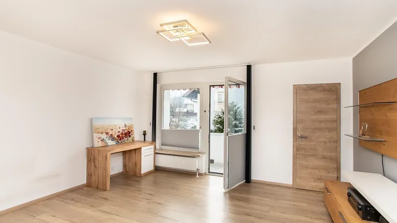 Geräumiges Wohnzimmer mit Holzboden, Schreibtischbereich und Zugang zum Außenbereich.