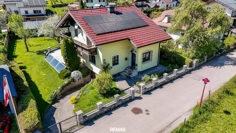 Vogelperspektive eines Einfamilienhauses mit rotem Ziegeldach, Solaranlage und gepflegtem Garten.