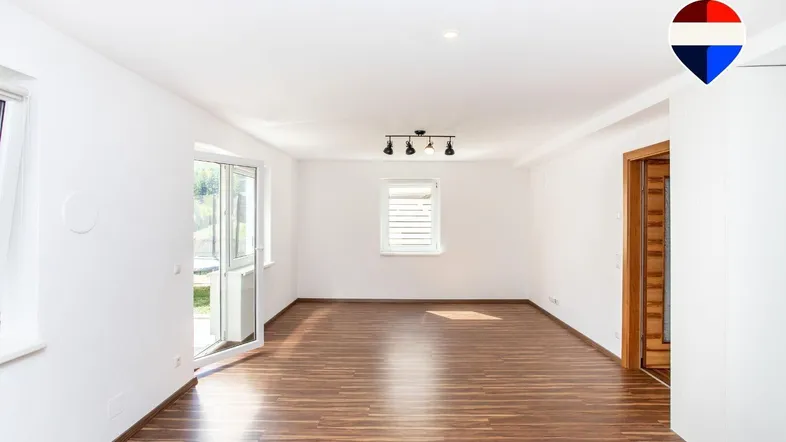 Helles, leeres Zimmer mit Laminatboden und Zugang zu einem Außenbereich durch eine Glastür.