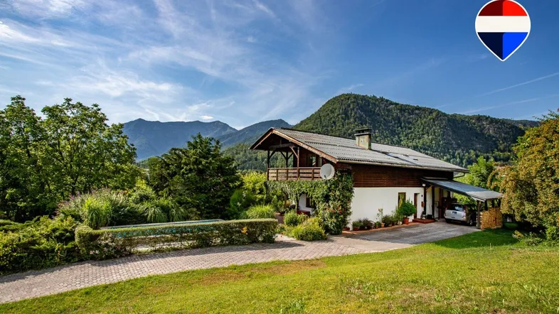Traditionelles Haus mit Holzfassade und großem Garten vor alpiner Bergkulisse.