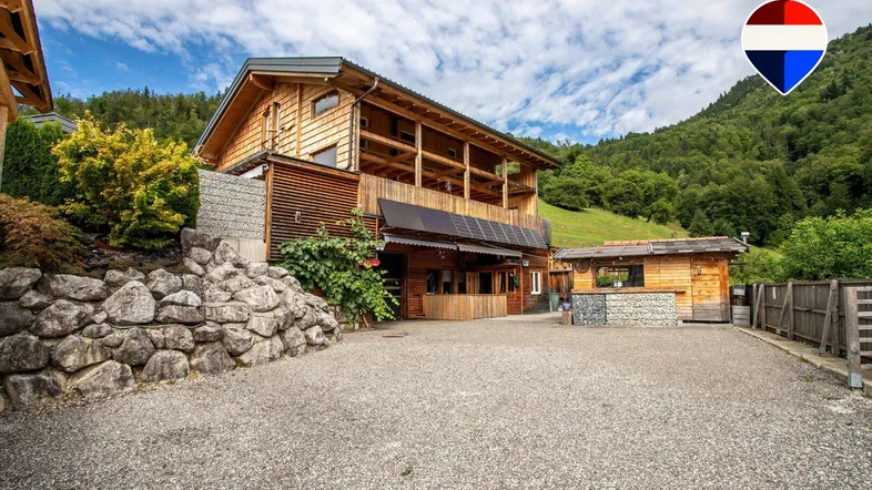 Rustikales Holzhaus mit großem Kiesparkplatz und umgeben von grünen Hügeln.