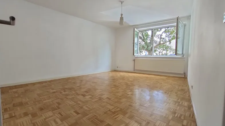Helles Zimmer mit Fischgrätparkettboden und Blick ins Grüne durch das geöffnete Fenster.