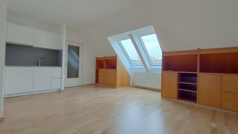 Helles Dachgeschosszimmer mit integrierter Küchenzeile, Holzboden und großen Dachfenstern für viel Licht.