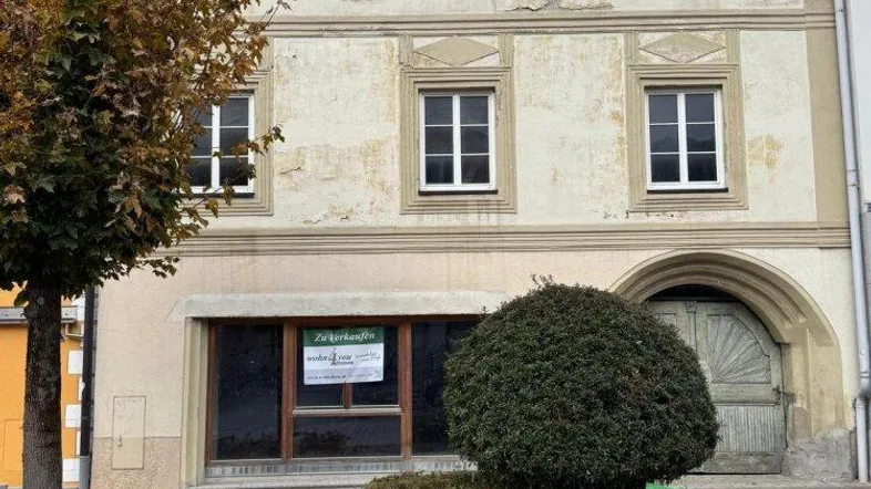 Altes Gebäude mit verputzter Fassade, Fenstern und einem großen Holztor im Erdgeschoss.