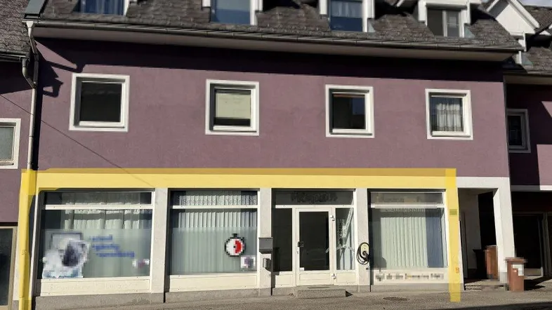 Ansicht der Gebäudefassade mit Satteldach und mehreren Fenstern, ein Geschäft im Erdgeschoss.