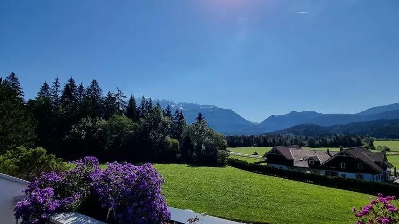 Blühende Terrasse mit bunten Blumen und idyllischem Blick auf grüne Wiesen und Berge.