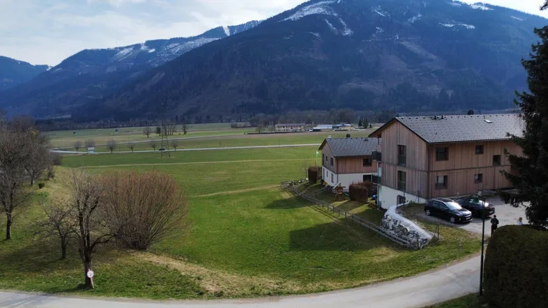 Blick auf die ländliche Umgebung mit Wohnhäusern, grünen Feldern und majestätischen Bergen im Hintergrund.
