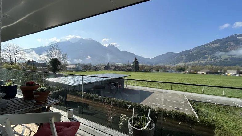 Geräumiger Balkon mit Holzboden, Glasgeländer und weitem Blick auf die Berge und grüne Landschaft.