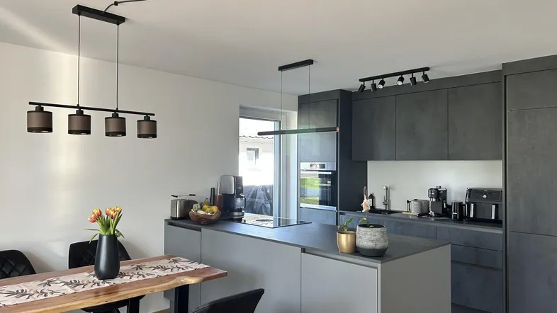 Offene, moderne Küche mit Essbereich, dunklen Schränken und einer Kücheninsel.