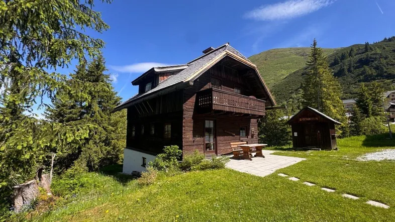 Seitenansicht des Holzchalets mit Balkon, gepflasterter Terrasse und Picknicktisch in Hanglage.