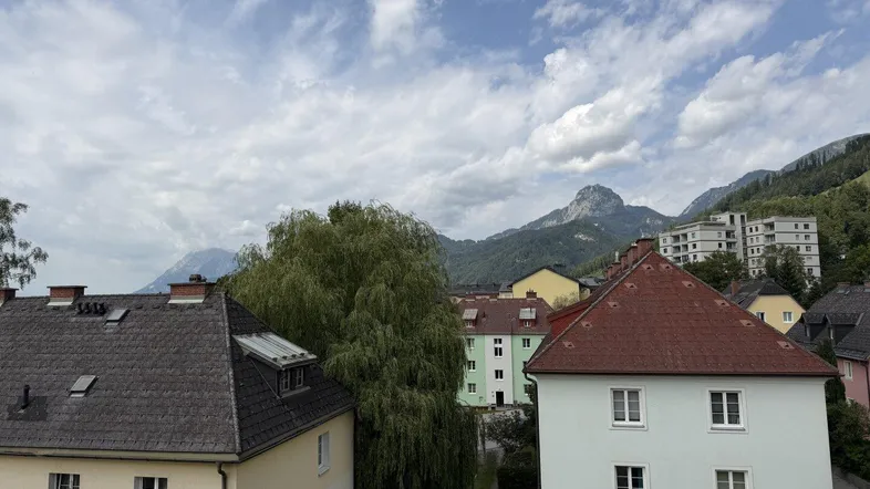 Blick auf Wohngebäude mit Bergen im Hintergrund unter bewölktem Himmel.