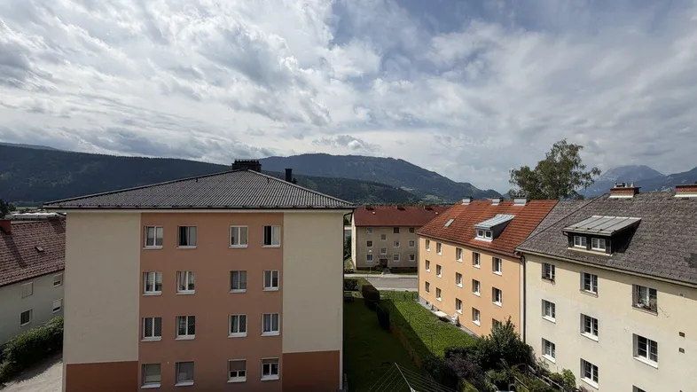 Wohngebäude mit Grünflächen, Wäscheleine und kleinem Pool vor einer Bergkulisse.