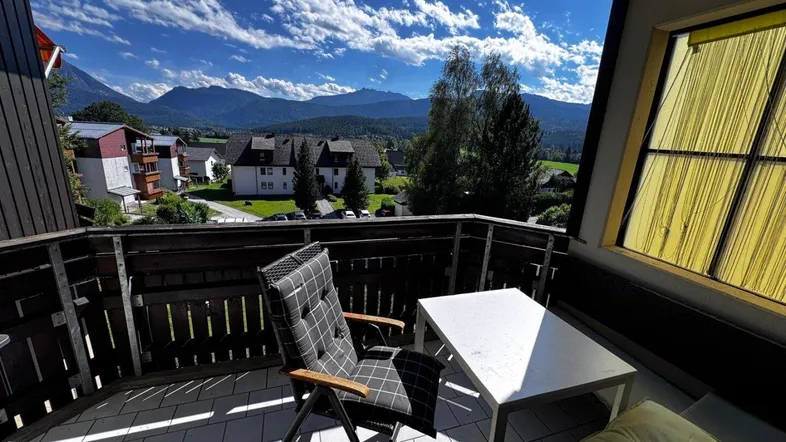 Gemütlicher Balkon mit Fliesenboden, Sitzgelegenheiten und atemberaubendem Bergblick unter blauem Himmel.