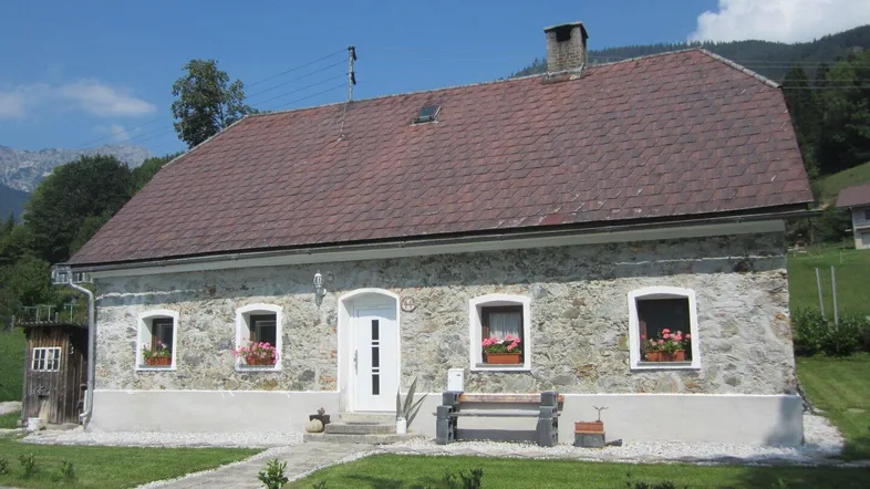 Traditionelles Steinhaus mit rotem Ziegeldach und Blumenkästen an den Fenstern in ländlicher Umgebung.