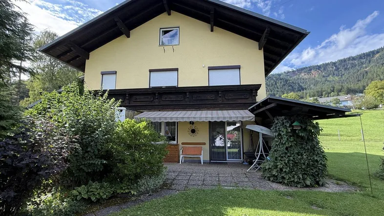 Eine gemütliche Terrasse am Haus mit Markise und Blick ins Grüne, umgeben von Pflanzen.