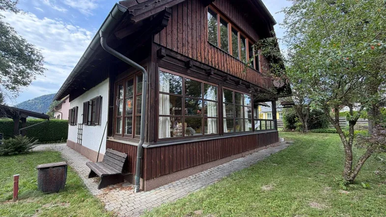 Traditionelles Holzhaus mit großen Fenstern und einem kleinen Gartenbereich mit Sitzbank.