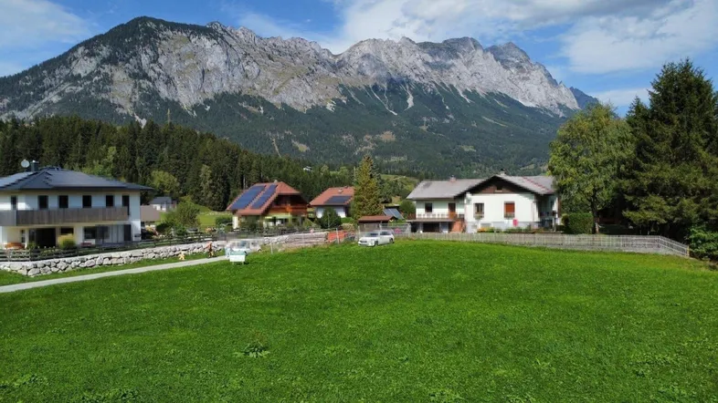 Ländliche Häuser mit Photovoltaikanlagen vor einer beeindruckenden Bergkulisse und grünen Wiesen.