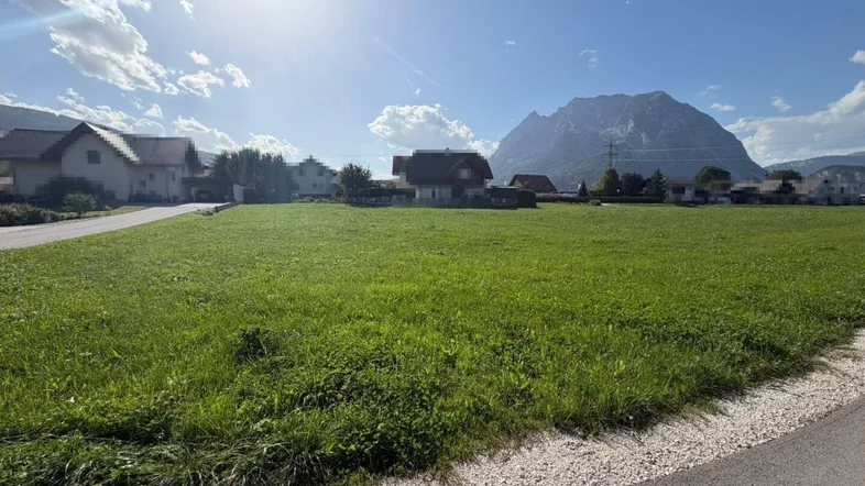 Großes grünes Grundstück mit weitem Blick auf die umliegende Berglandschaft unter strahlendem Sonnenschein.