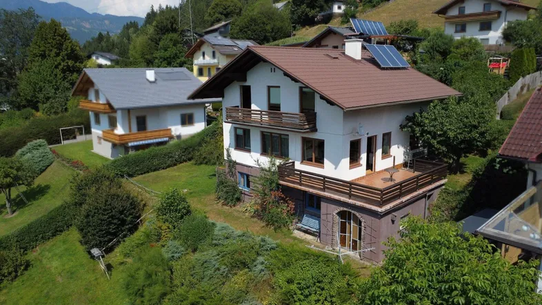 Freistehendes Haus in Hanglage mit mehreren Balkonen und Photovoltaikanlage auf dem Dach, umgeben von viel Grün.