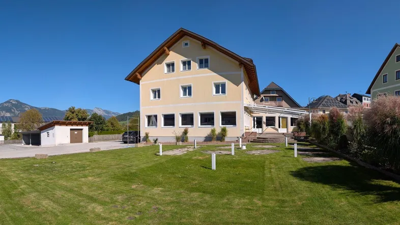 Großes Wohngebäude mit gelber Fassade, Satteldach und gepflegtem Rasen im Vordergrund.