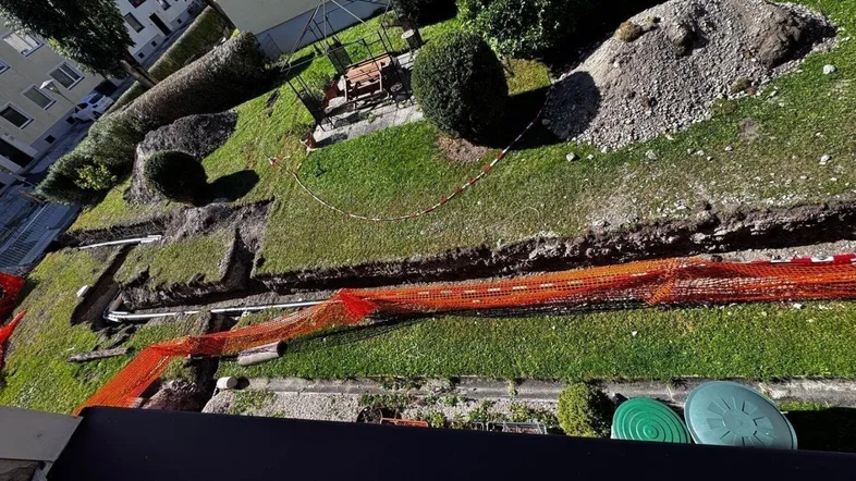 Gartenbereich mit Bauarbeiten, Gräben und Erdhügeln, umgeben von Grünflächen und Bäumen.