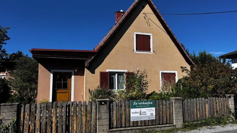 Traditionelles Einfamilienhaus mit beiger Fassade, Satteldach und Fensterläden, umgeben von einem gepflegten Vorgarten.
