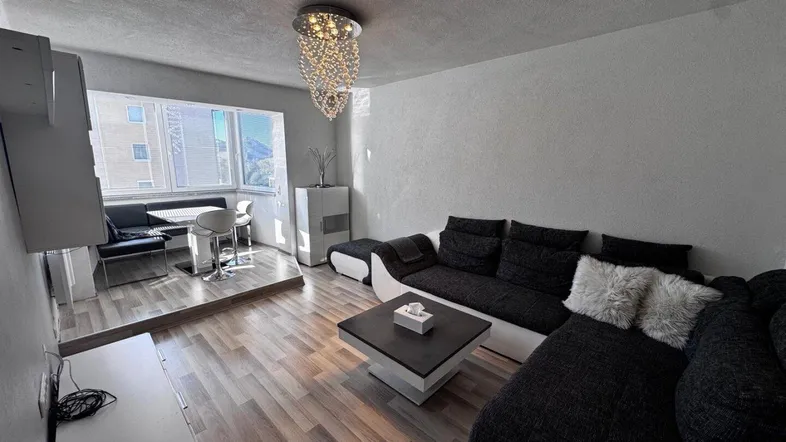 Helles Wohnzimmer mit modernem Sofa, Holzboden und einem erhöhten Essbereich mit Bergblick.