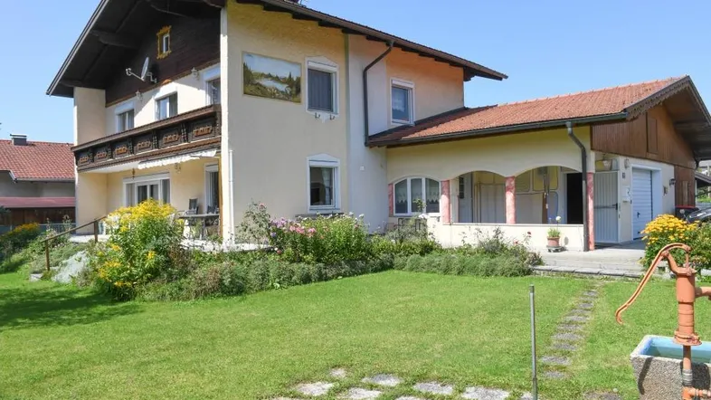 Traditionelles Haus mit gepflegtem Garten, Blumenbeeten und einer alten Wasserpumpe.