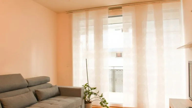 Helles Wohnzimmer mit gemütlichem Sofa, Holzboden und Zugang zu einem Balkon.