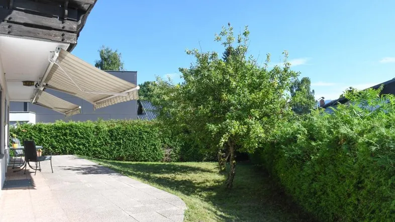 Sonnige Terrasse mit ausfahrbarer Markise, umgeben von einem gepflegten Garten und grünen Hecken.