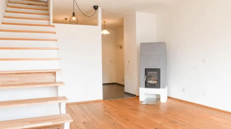 Helles Wohnzimmer mit Holzboden, Kamin und offener Treppe zum Obergeschoss.