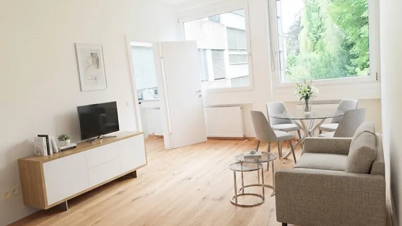 Helles Wohn- und Esszimmer mit Holzboden, großen Fenstern und moderner Einrichtung.