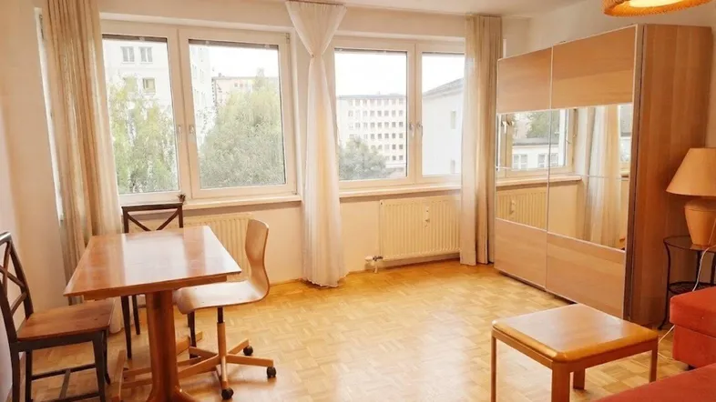 Helles Wohnzimmer mit Parkettboden, Esstisch und großem Fenster mit Blick ins Grüne.