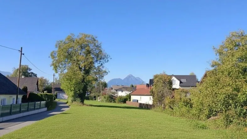 Weitläufige Grünfläche mit Blick auf die umliegende Berglandschaft und benachbarte Häuser unter blauem Himmel.