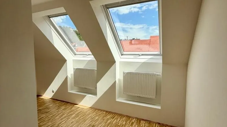 Helles Dachgeschosszimmer mit Holzboden, zwei Dachfenstern und Heizkörpern.