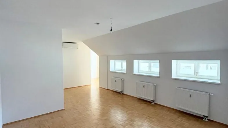 Helles Dachzimmer mit Parkettboden und mehreren Fenstern, ideal als Wohn- oder Schlafbereich.