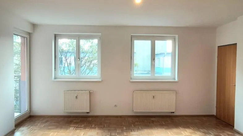 Helles, leeres Zimmer mit Fischgrätparkettboden und zwei Fenstern, bereit zur individuellen Gestaltung.