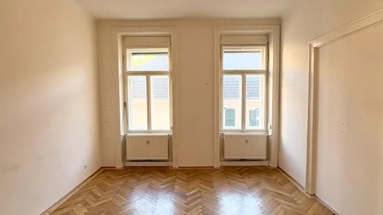 Helles Zimmer mit Fischgrätparkettboden und zwei Fenstern, ideal als Wohn- oder Schlafzimmer.